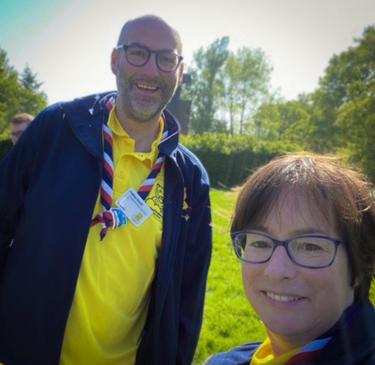 A picture of Matt and Kester. Matt is a tall man wearing glasses with a yellow t shirt and navy, white and red knacker. Kester is a woman with short brown hair and glasses. They are both smiling.